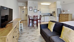 Ein kleines Hotelzimmer mit Fernseher, einem Holzschrank, einer Couch und einer Küchenzeile.