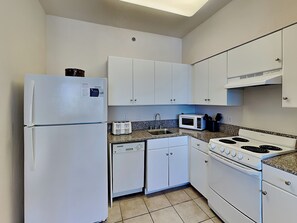 A compact kitchen with white cabinets, a refrigerator, a microwave, a toaster, a sink, and a stove.