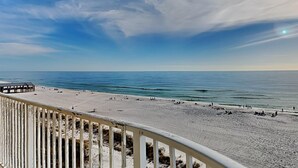 A beach view from a balcony with a railing, a sandy beach, and the ocean.