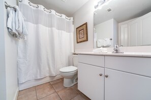 Un baño con inodoro, lavabo con espejo, cortina de ducha y toallero.