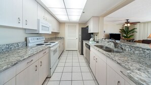 Eine moderne Küche mit weißen Schränken, Granit Arbeitsplatten, einer Mikrowelle, einem Herd, einem Kühlschrank, einem Geschirrspüler und einem Deckenventilator.