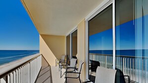 Un balcon avec vue sur l’océan, doté d’une balustrade, de chaises et d’une porte vitrée.