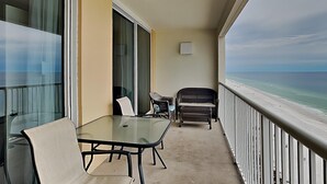 A balcony with a glass table and chairs, a view of the beach, and a white railing. - Gulf Front Condo with Incredible Views and Resort Amenities (Panama City Beach)