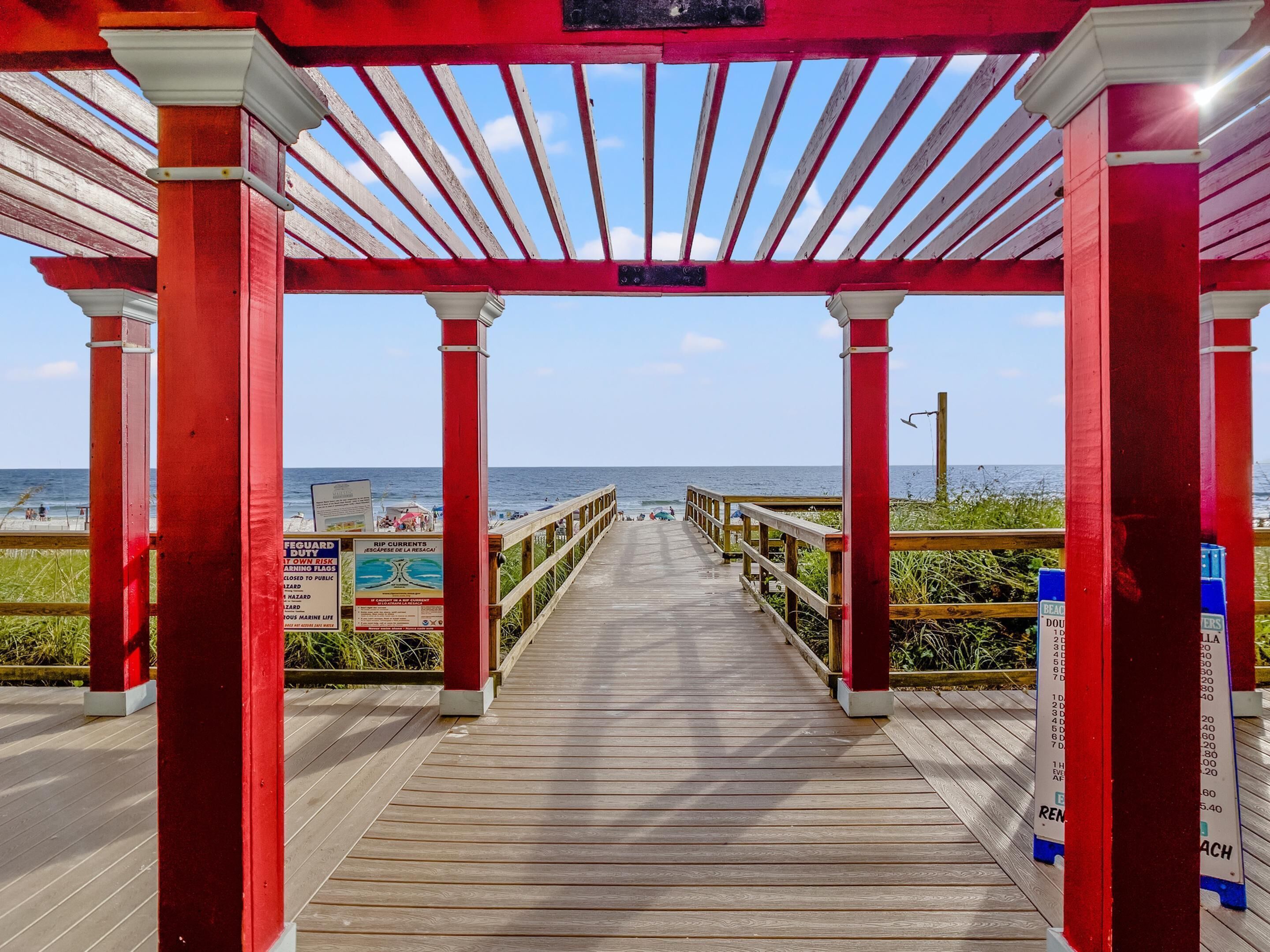 A wooden boardwalk leading to the beach with red pillars and a clear view of the ocean.