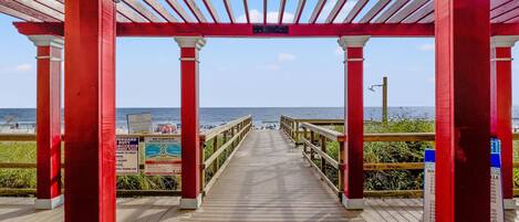 A wooden boardwalk leading to the beach with red pillars and a clear view of the ocean.