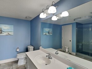 A bathroom with a large mirror, white sink, and two toilets.