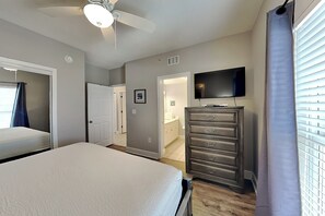 A bedroom with a bed, a dresser, a ceiling fan, and a television.