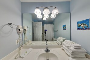 A bathroom with a sink, mirror, towel stack, and hair dryers.