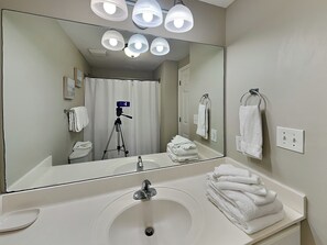 Un baño con un espejo grande, lavamanos blanco y varias toallas.
