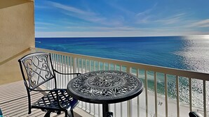 A balcony with a round table and chairs, overlooking a beach with clear blue water and a bright sky. - Majestic Beach Towers I #1410 | Gulf Front + Amenities (Panama City Beach)