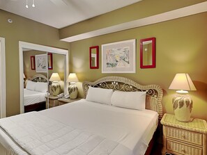 A neatly made bed with white linens in a room with green walls, two bedside tables with lamps, and two framed pictures on the wall.