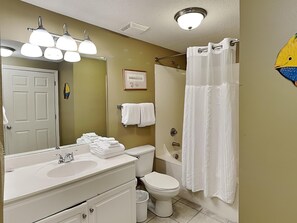 A bathroom with a sink, toilet, and shower. There is a towel rack with towels, a framed certificate on the wall, and a fish decal on the wall.