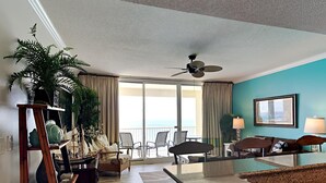 A hotel room with a balcony, a dining area, and a seating area with a view of the ocean.