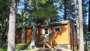 A wooden cabin with a staircase leading to a door, surrounded by trees.
