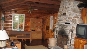 A cozy cabin interior with a stone fireplace, wooden furniture, and a television.