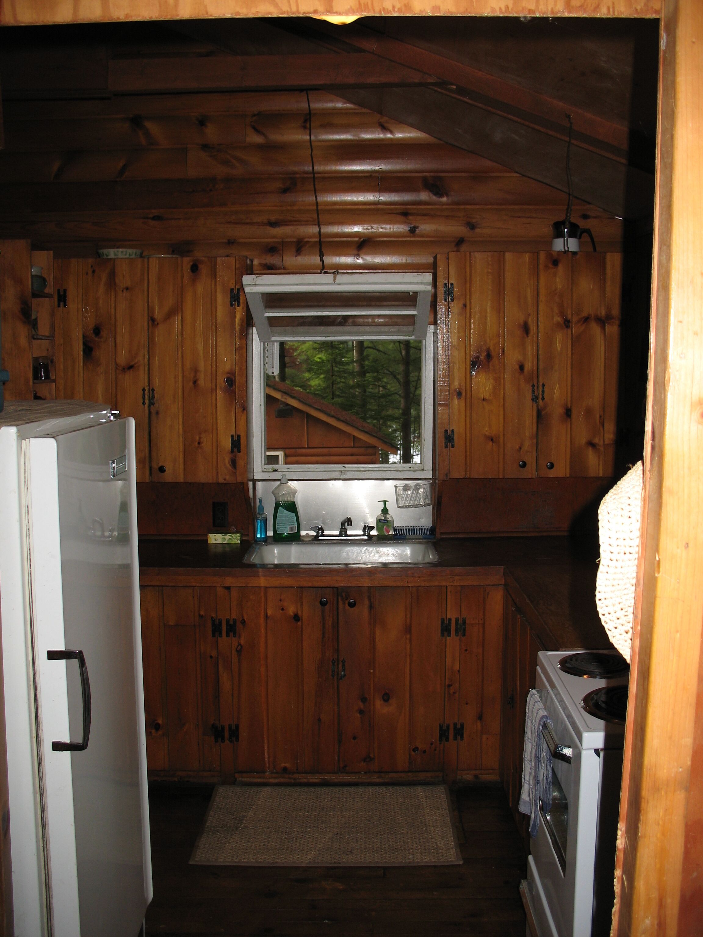 A compact kitchen with wooden cabinets, a sink, a refrigerator, and a stove.