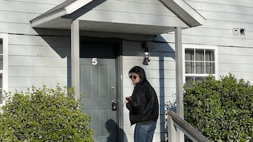 A person exiting a house with a grey door and a small porch.