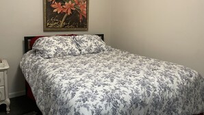 A bedroom with a bed, a nightstand, and a framed botanical print on the wall. - Vacation Condo #5 2BR with full kitchen, walk to river and shops, pets welcome (Hardy)