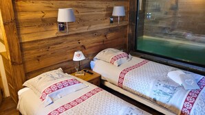 A room with wooden walls, two beds with patterned bedding, bedside lamps, a nightstand with a book and remote, and a window with a view. - Chalet de prestige 18 people swimming pool jacuzzi sauna (Vars)