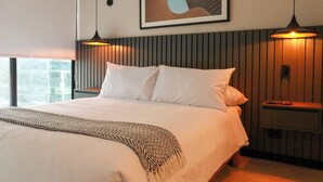 A modern hotel room with a large bed, a wooden headboard, and two pendant lights.