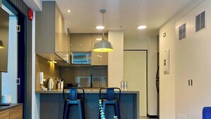 A modern kitchen with two bar stools, a microwave, and a hanging pendant light.