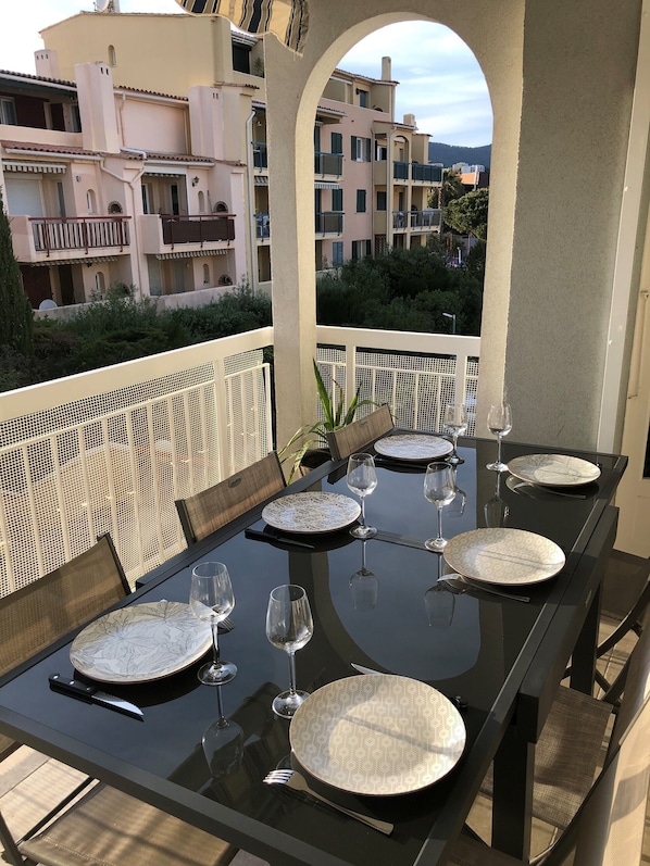 Een terras met een zwarte tafel gedekt voor zes personen, omringd door rieten stoelen.
