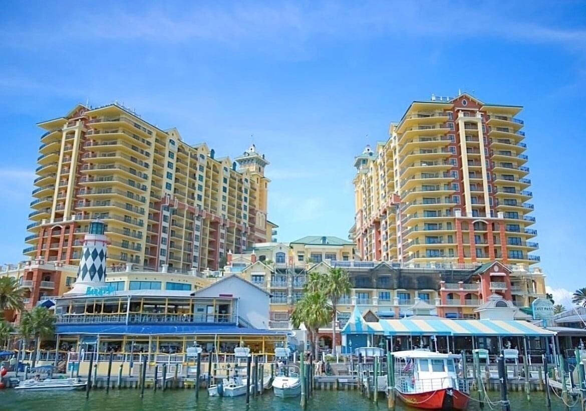 A marina with boats docked, surrounded by high-rise hotels with balconies and a clear sky.