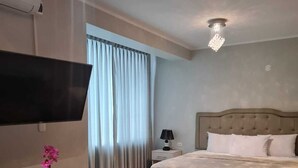 Ein Hotelzimmer mit Bett, Fernseher, Schreibtisch mit Stuhl und einem Fenster mit Vorhängen.