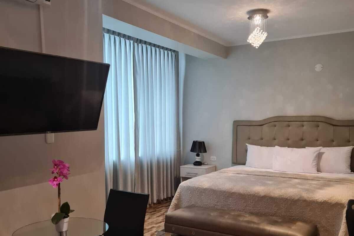 Une chambre d’hôtel avec un lit, une télévision, un bureau avec une chaise et une fenêtre avec des rideaux.