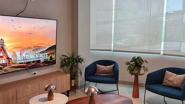 Ein modernes Wohnzimmer mit Fernseher, zwei blauen Sofas, einem Holztisch und einem großen Fenster.