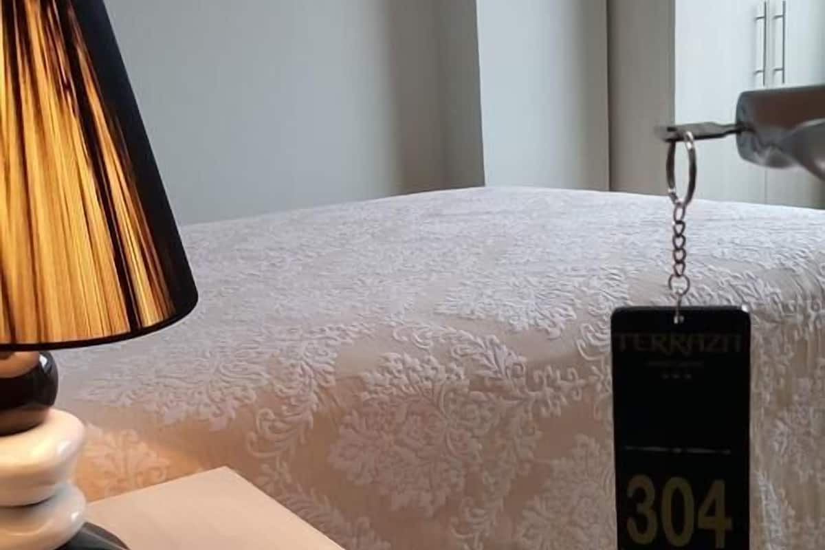 Une chambre d’hôtel avec un lit, une table de chevet avec une lampe et une étiquette accrochée au lit.