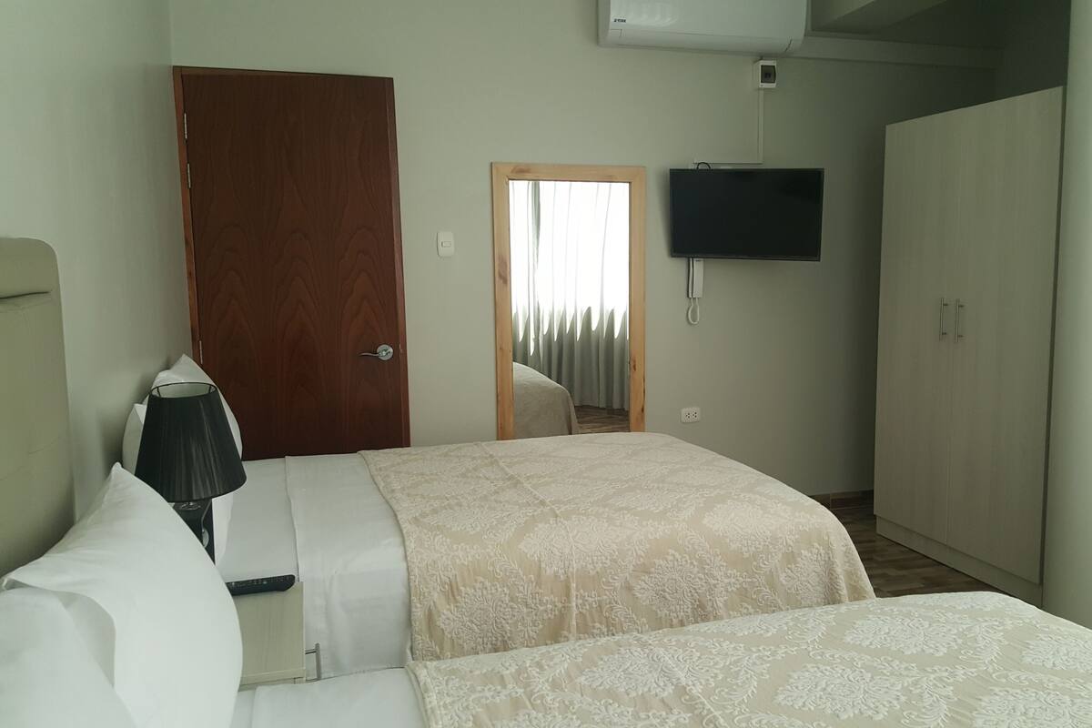 Une chambre d’hôtel avec deux lits, un téléviseur fixé au mur, une armoire et une porte.