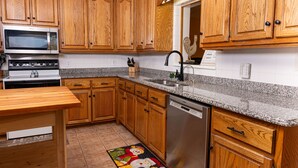 A kitchen with wooden cabinets, a stainless steel dishwasher, a granite countertop, and a microwave. - Farmhouse on Beautiful Bison Farm (Opelika)