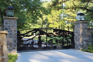 A gated entrance with a metal gate featuring a tree and animal silhouette design, flanked by stone pillars with lanterns.