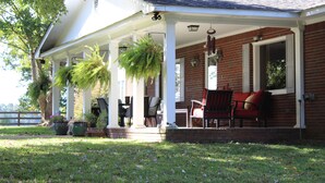 A covered porch with outdoor seating, potted plants, and a brick exterior. - Farmhouse on Beautiful Bison Farm (Opelika)