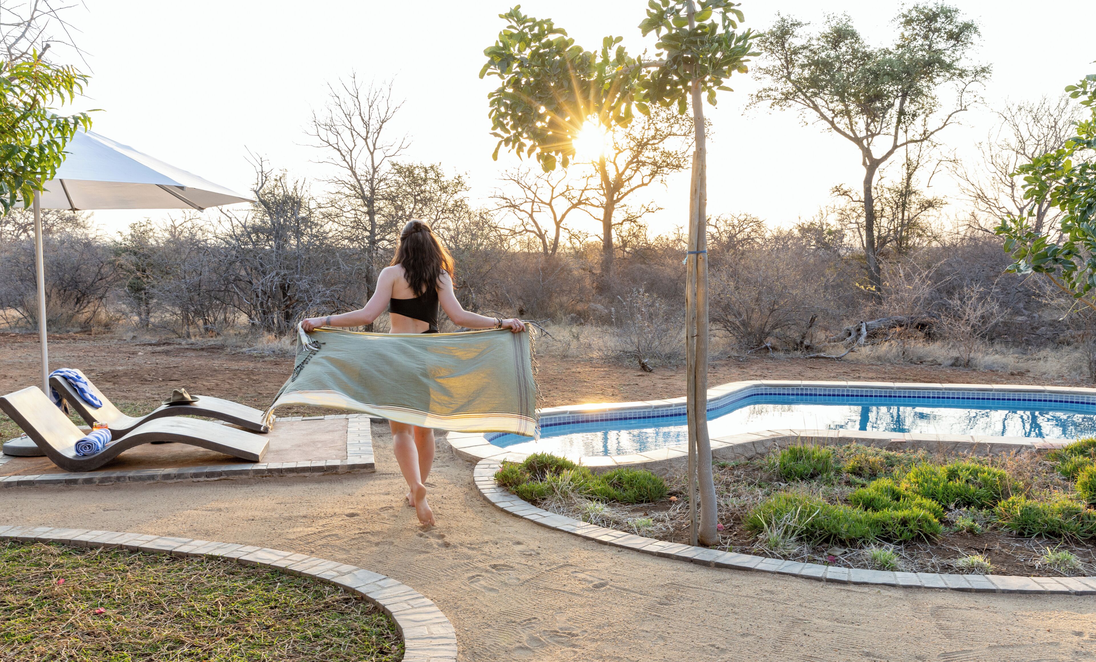 Uma área de piscina com espreguiçadeiras, piscina e uma pessoa segurando uma toalha.
