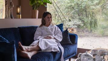 A person sitting on a blue sofa in a room with a window overlooking a garden.