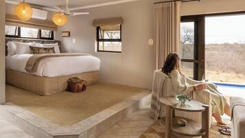 A bedroom with a large bed, a small table, and a view of the outdoors.