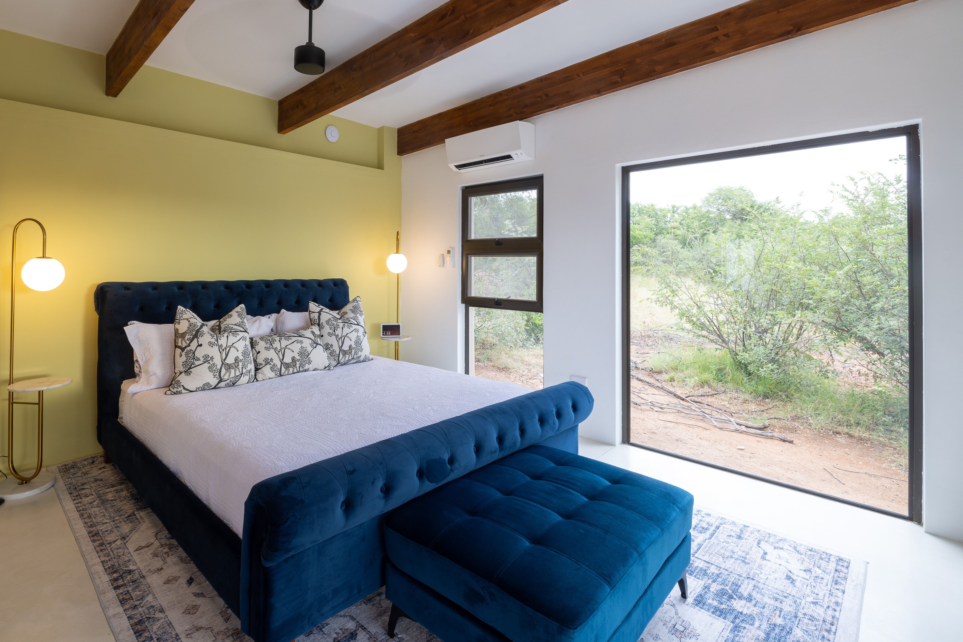 Un dormitorio con una cama grande, un banco, una lámpara de noche y vistas al exterior.