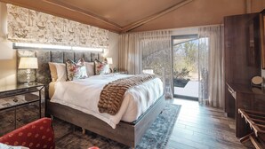 Een slaapkamer met een groot bed, een nachtkastje, een rode stoel, een houten bureau en uitzicht op de buitenlucht door een schuifdeur.