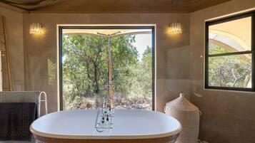 A modern bathroom with a freestanding bathtub, a large window, and a view of trees.