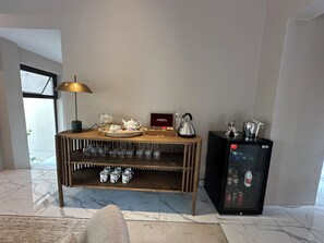 A room with a wooden coffee table, a glass display case, a kettle, a teapot, a refrigerator, and a coffee machine.