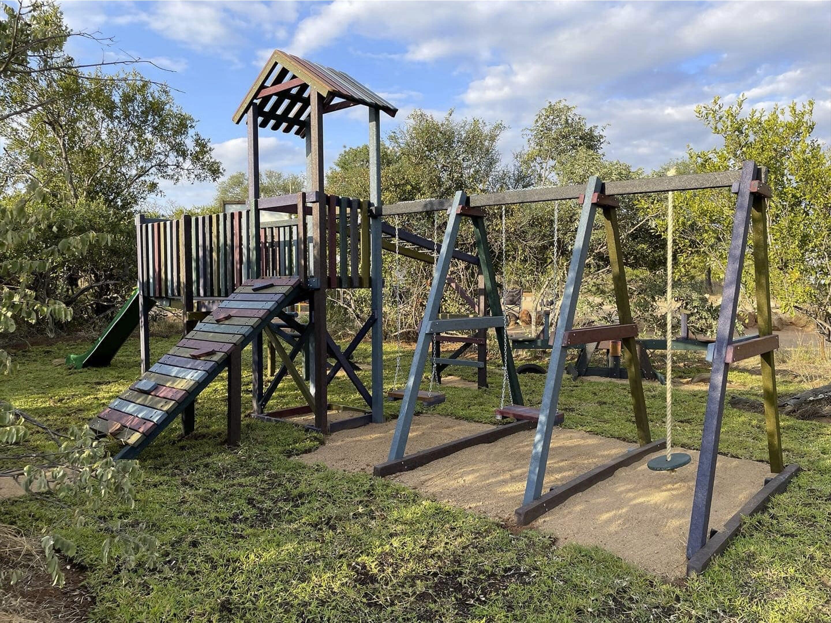 A wooden playground structure with a slide, swings, and a climbing area.