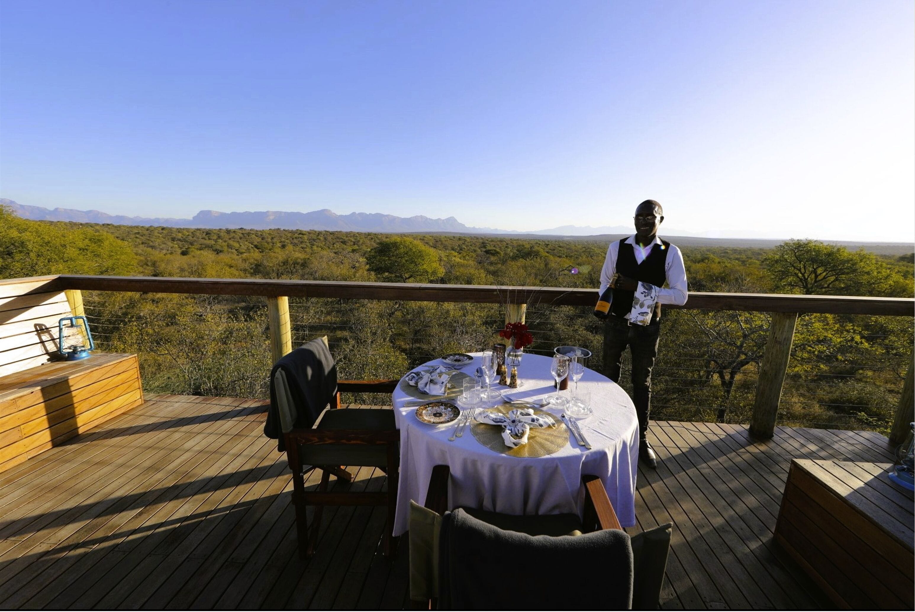 A dining table set on a wooden deck with a view of a mountainous landscape.