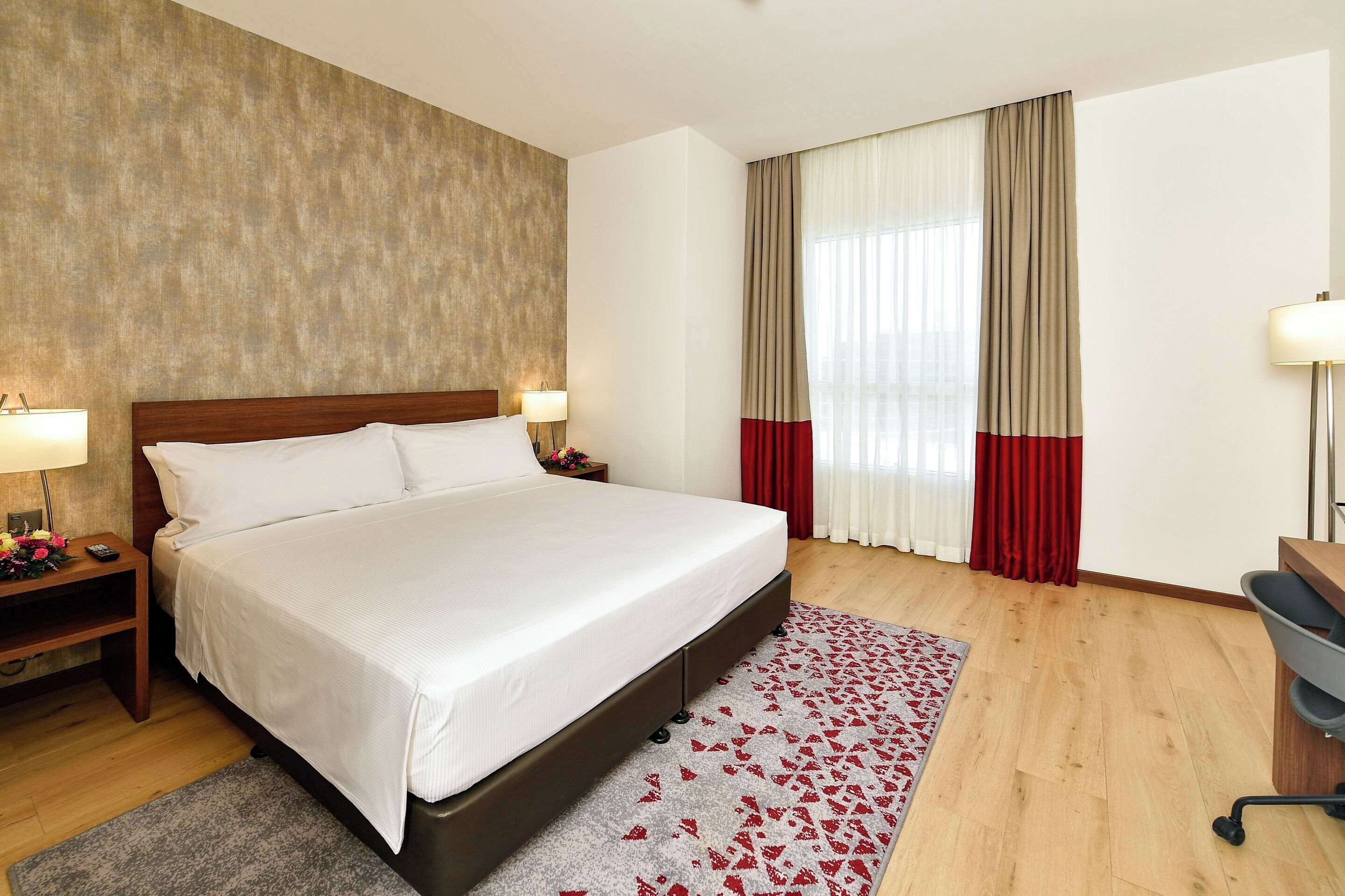 Habitación de hotel con una cama grande, cabecero de madera, mesitas de noche con lámparas, un escritorio y una silla.