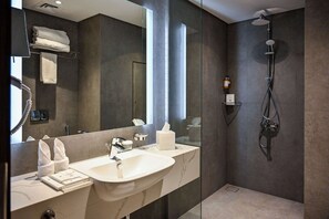 A modern bathroom with a large mirror, two sinks, a shower, and a towel rack.