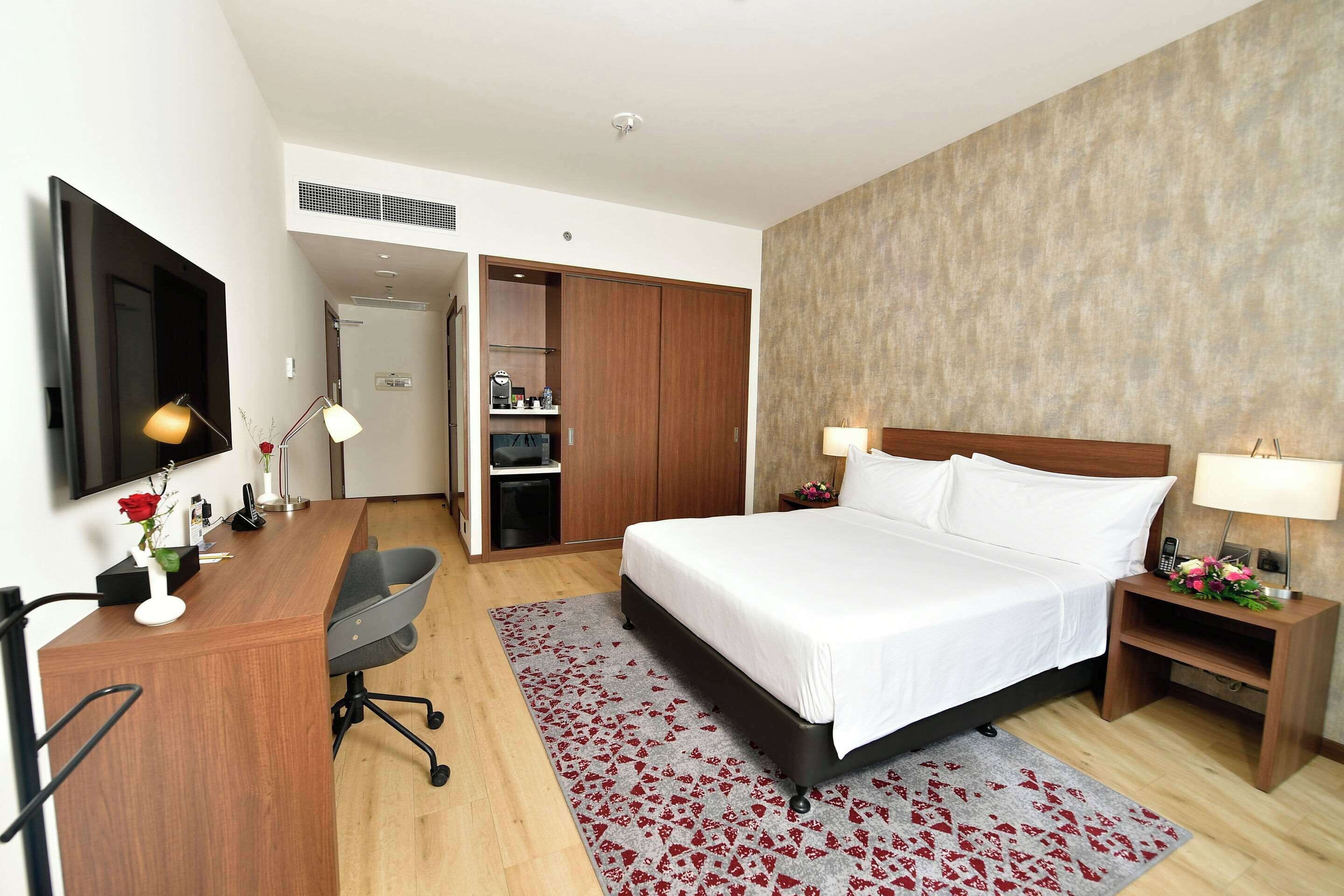 A hotel room with a bed, desk, chair, and a TV on the wall.