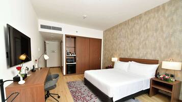 A hotel room with a bed, desk, chair, and a TV on the wall.