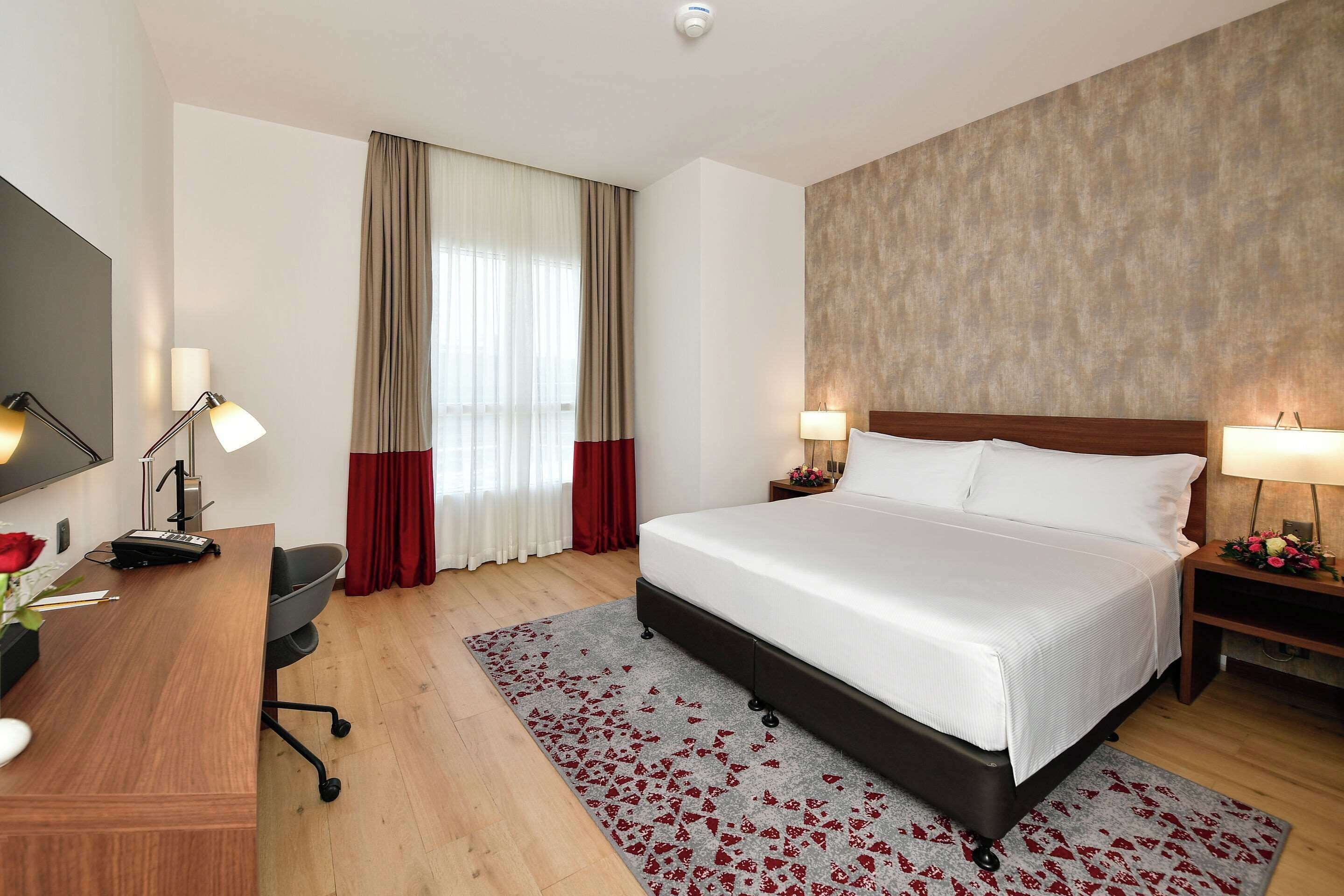 A hotel room with a large bed, a desk with a chair, a TV, and a window with curtains.