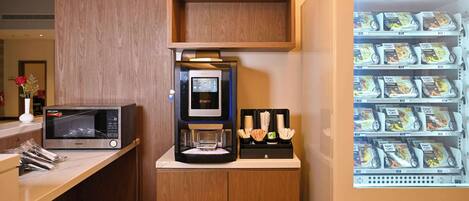 A kitchenette with a microwave, coffee machine, and a beverage dispenser.